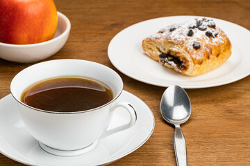 Hot black coffee in white ceramic cup on ceramic saucer for breakfast with Danish Pastry filled...