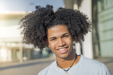 Young handsome black African American man looking at camera smiling in the campus during a sunny day.
