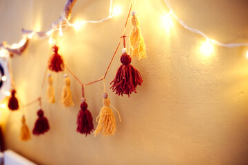 Cozy homemade garland from pompons from threads on the wall in the room, home decor Scandinavian style, mustard and brown, recycling