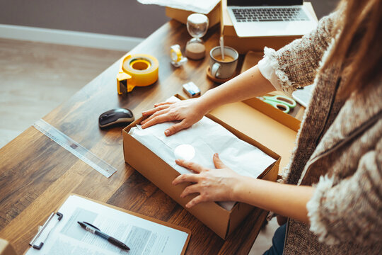 Young woman, owener of small business packing product in boxes, preparing it for delivery. Women packing package with her products that she selling online. Female entrepreneur working at home office