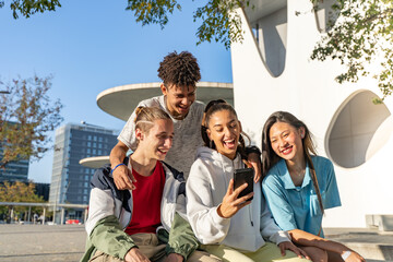 Group of happy teenage friends looking the phone and laughing in the city street.