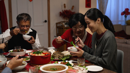 happy asian grandmother and daughter in law giving food to each other while eating dinner together on the eve of Chinese new year at a cozy home interior.