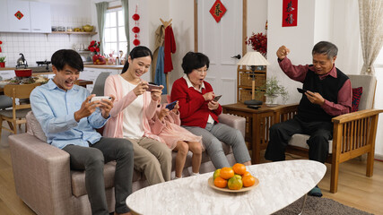 excited family of mixed generations cheering with hand gestures as they are playing mobile games at home during new year's holiday. translation of chinese words: spring and congratulation