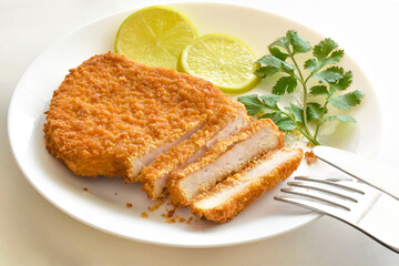 Chicken schnitzel with coriander and lime on a white plate. 