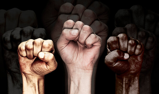 Hands of people of different nationalities and skin colors clenched into fists on a black background with reflection. The concept of combating racism, tolerance and emigration.