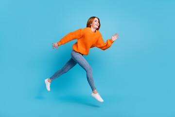 Fototapeta na wymiar Photo of sweet adorable young woman wear orange sweater jumping high running fast smiling isolated blue color background