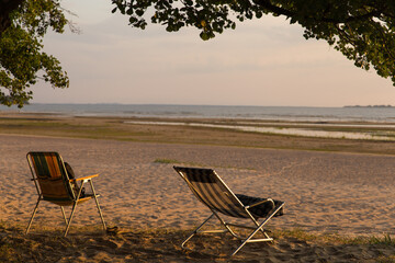 two camping chairs stand on the seashore empty without people in the setting sun in summer