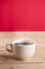 broken white coffee cup with hot steam smoke on rustic wooden table, red background