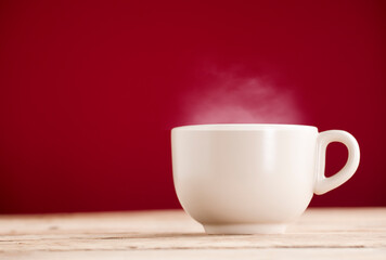broken white cup of tea or coffee with hot steam smoke on rustic wooden table, red background