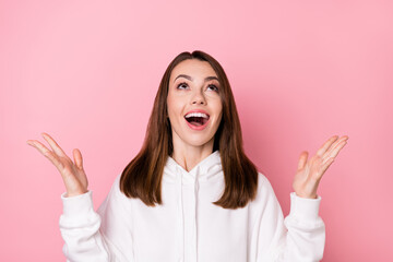 Photo of shocked excited young woman look up empty space hold hands isolated on pastel pink color background