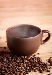 Brown cup of coffee with smoke on rustic wooden table, with roasted coffee beans