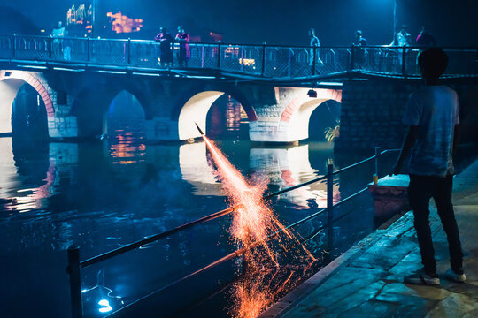 A boy lighting fireworks. Fireworks sparks reflecting in the lake. People watching fireworks from the bridge at Pichola Lake, Udaipur, Rajasthan, India. 