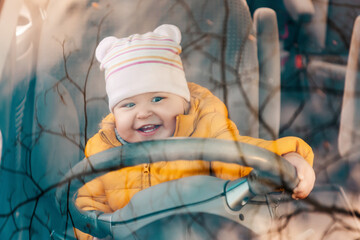 Portrait of little happy child is sitting at the wheel of a car. View through the windshield of the...