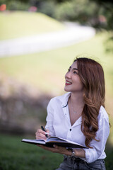 Obraz premium Joyful casual Asian student girl with laptop outdoors. Smiling woman sitting on the grass with a computer, surfing the net or preparing for exams. Technology, education and remote working concept