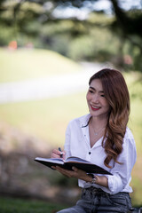 Obraz premium Joyful casual Asian student girl with laptop outdoors. Smiling woman sitting on the grass with a computer, surfing the net or preparing for exams. Technology, education and remote working concept