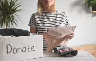 Young woman stands at a table in room and puts clothes in a donation box. Clothes Donation,...