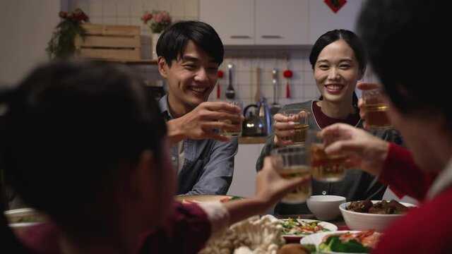 selective focus of happy young asian couple drinking toast with tea to their family at chinese chinese lunar new year reunion dinner at home. chinese text translation: fortune
