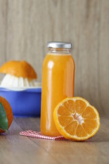 Mandarin juice, close up on glass bootle of homemade mandarin or tangerin juice and selective focus on mandarin slice. Blue squeezer on wooden texture background. vertical shooting. 