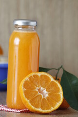 Mandarin juice, close up on glass bootle of homemade mandarin or tangerin juice and selective focus on mandarin slice. Blue squeezer on wooden texture background. vertical shooting. 