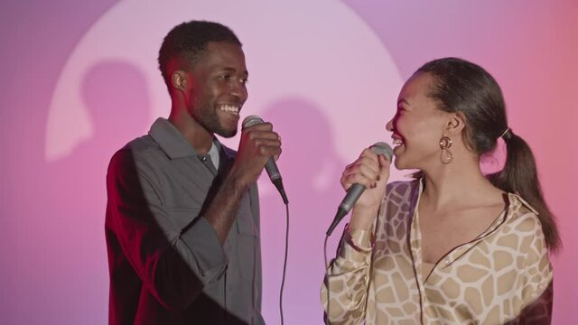 Medium slowmo shot of young happy African-American couple singing together in karaoke looking at each other