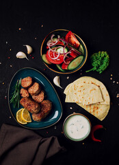 Traditional Cypriot Seftalia dish, grilled, with vegetables, pita, and sauce, top view, on a black background, no people,