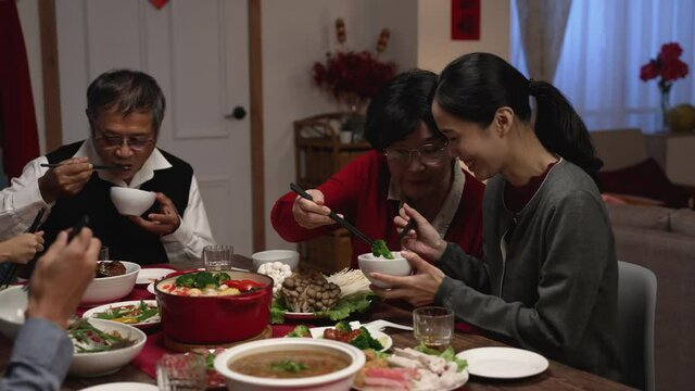 happy asian grandmother and daughter in law giving food to each other while eating dinner together on the eve of chinese lunar new year at a cozy home interior.