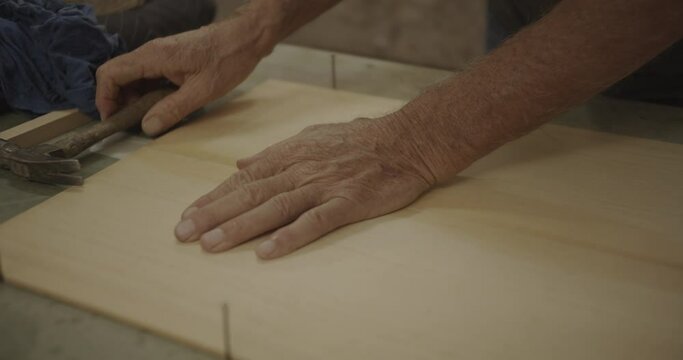 Old hands tap a hammer over glued wood