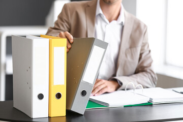 Young man with folders at table in office, closeup