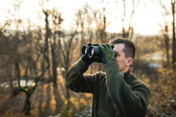 Professional hunter looking through binoculars. Man on the hunt in the middle of forest. 