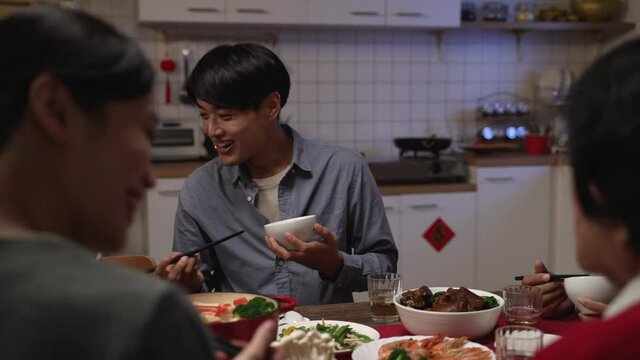selective focus smiling asian father talking to family while enjoying tasty food at dinner table. people chatting happily during reunion meal on chinese lunar new year's eve at home