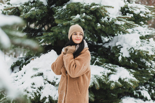 A beautiful girl in a brown fur coat near a snow tree.