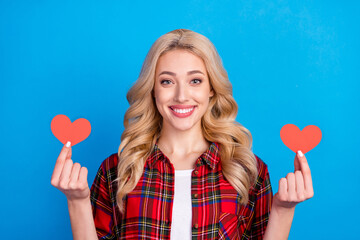 Photo of charming sweet young woman dressed checkered shirt smiling holding two red hearts isolated blue color background