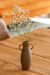 Vase with gypsophila flowers on wooden table in living room