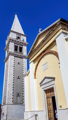 Obraz premium A view on a church and a bell tower from the bottom. The walls of the church are painted yellow, and bell tower's are painted grey. Buildings nicely contrasted with a clear blue sky.
