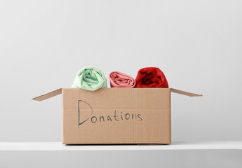 Cardboard box with donation clothes on shelf against light background