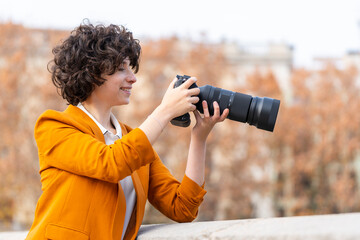 Young brunette woman with curly hair taking a picture with telephoto lens