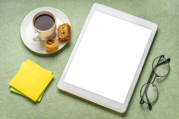 mockup of digital tablet with a blank isolated screen (clipping path included) with coffee, baklava, and reading glasses against handmade paper