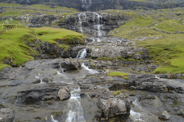 Naklejka na ściany i meble The white streaming waterfalls over the black lava rocks on the Faroe Islands in the Atlantic
