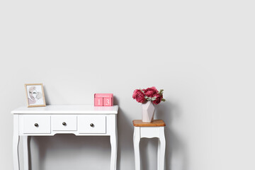 Tables with flowers in vase, picture and cube calendar near light wall