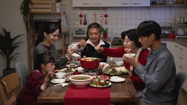 happy asian family members picking food from hot pot with chopsticks while enjoying traditional reunion dinner at home on chinese lunar new year's eve
