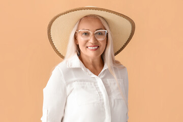 Mature woman in stylish hat wearing eyeglasses on color background