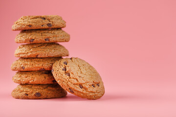 Oatmeal cookies with chocolate are stacked on a pink background.