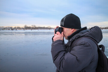 A man takes pictures with a film camera in winter in cold weather. The photographer looks into the viewfinder of the camera to photograph the winter landscape.