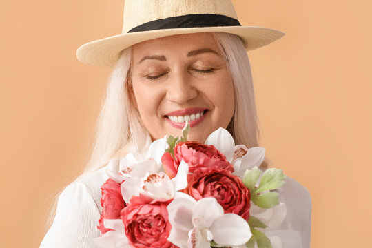 Smiling mature woman with closed eyes holding bouquet of beautiful flowers on color background