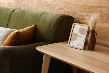 Vase with dry reeds and picture on wooden coffee table in living room