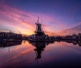 Fototapeta na wymiar Beautiful sunrise with pink and orange clouds at the Adriaan windmill along the Spaarne river in Haarlem, reflected in the water