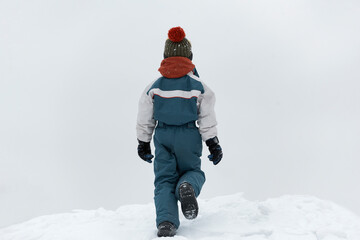 Fototapeta na wymiar Back view the child walks in the winter on the street. Boy walks on loose snow. Cold winter day.