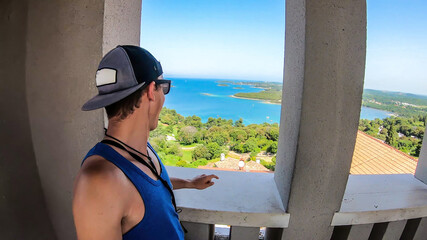 Young man looking through the window of bell tower on the harbor. Rows of docks waiting for the...