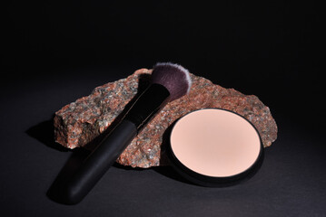 Makeup brush and compact pressed powder lie on granite stone on black background