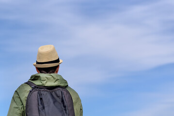 Back view of a man in a hat with a backpack on a blue sky background with copy space for text.